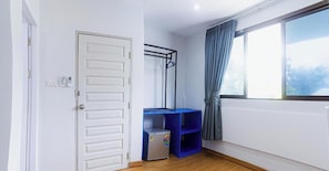 A room with a white door, a window with curtains, a blue shelf unit, and a small refrigerator. - Silla Patong Boutique – Beach Walk Access (Patong)