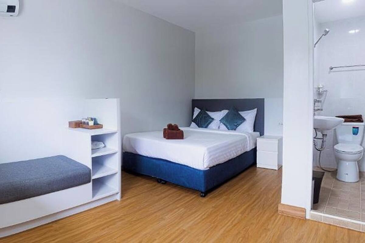 A compact hotel room with a bed, a small seating area, a bedside table, and a shower area.