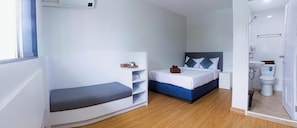 A compact hotel room with a bed, a small seating area, a bedside table, and a shower area. - Silla Patong Boutique – Beach Walk Access (Patong)