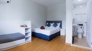 Una habitación de hotel compacta con cama, mesitas de noche, un rincón de descanso y una ducha.