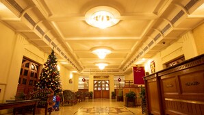 Un amplio vestíbulo con un gran árbol de Navidad, muebles de madera y un cartel rojo.