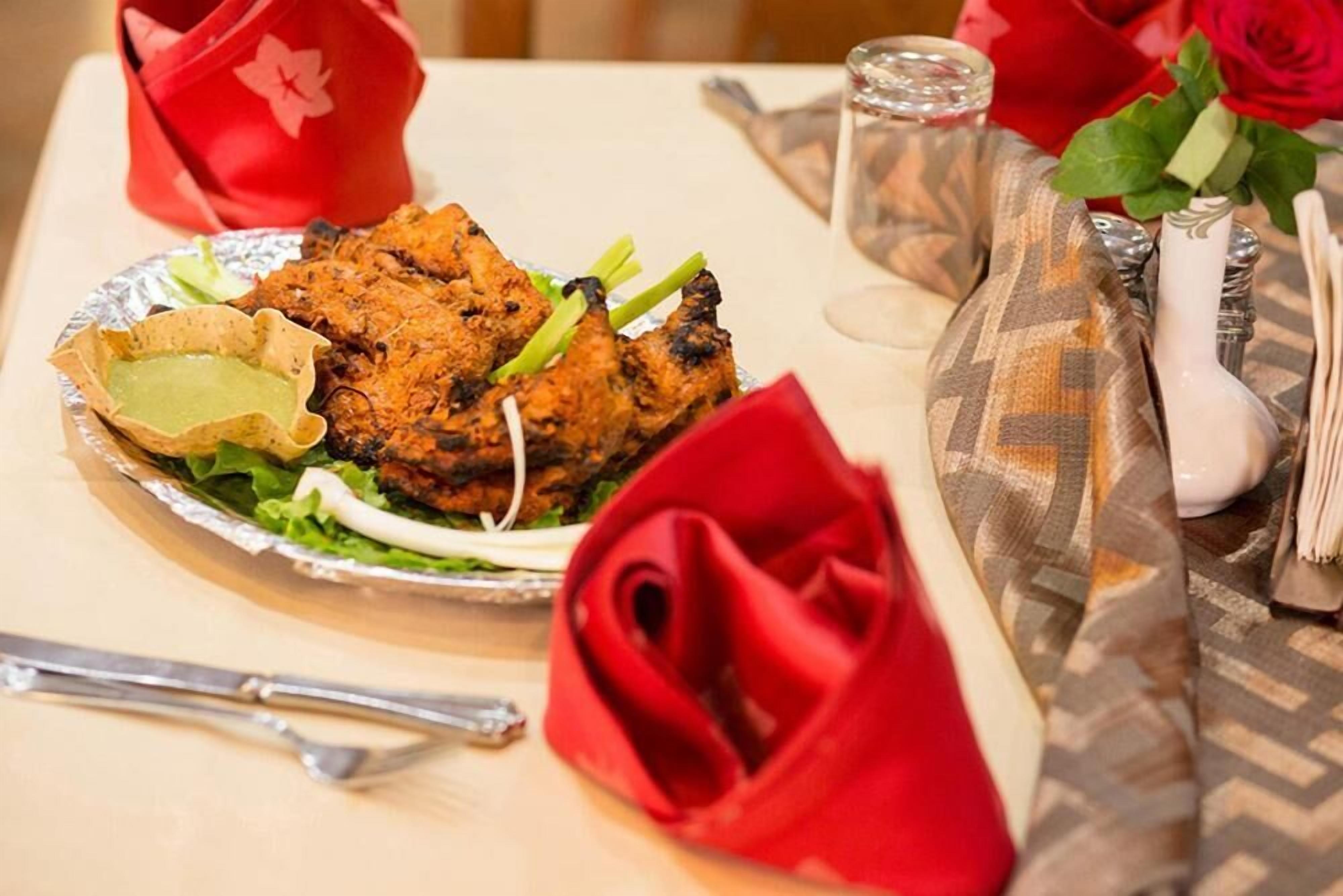 A table set with a meal, including grilled meat, salad, and a green sauce, with red napkins and a rose.