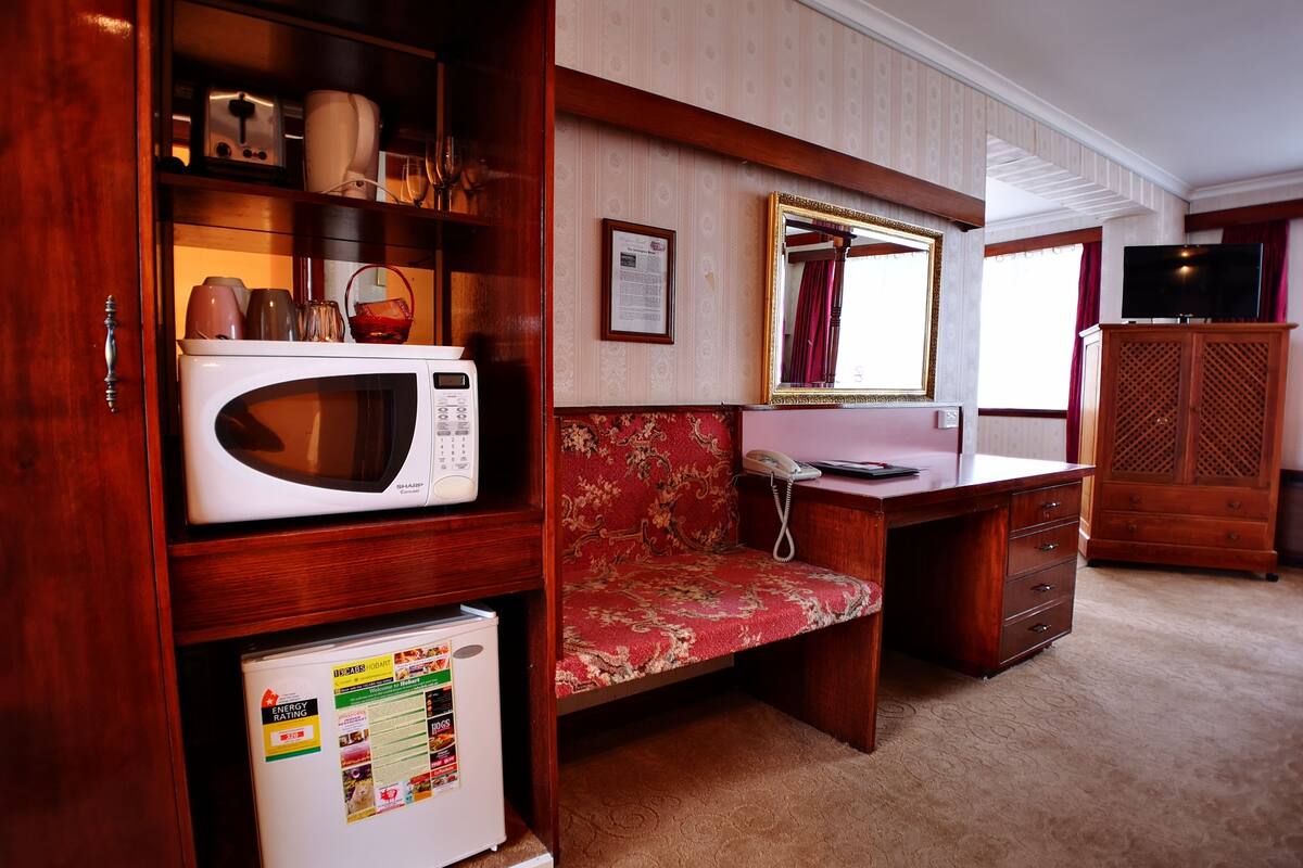 A compact room with a microwave, a small refrigerator, a telephone, a wooden cabinet, and a television.