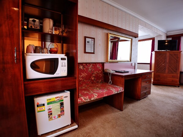 Una habitación compacta con microondas, refrigerador pequeño, teléfono, mueble de madera y televisor.