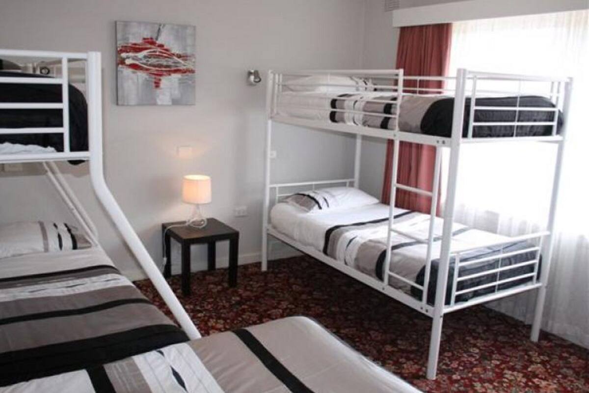 A bunk bed room with a small table and lamp, a painting on the wall, and a window with curtains.