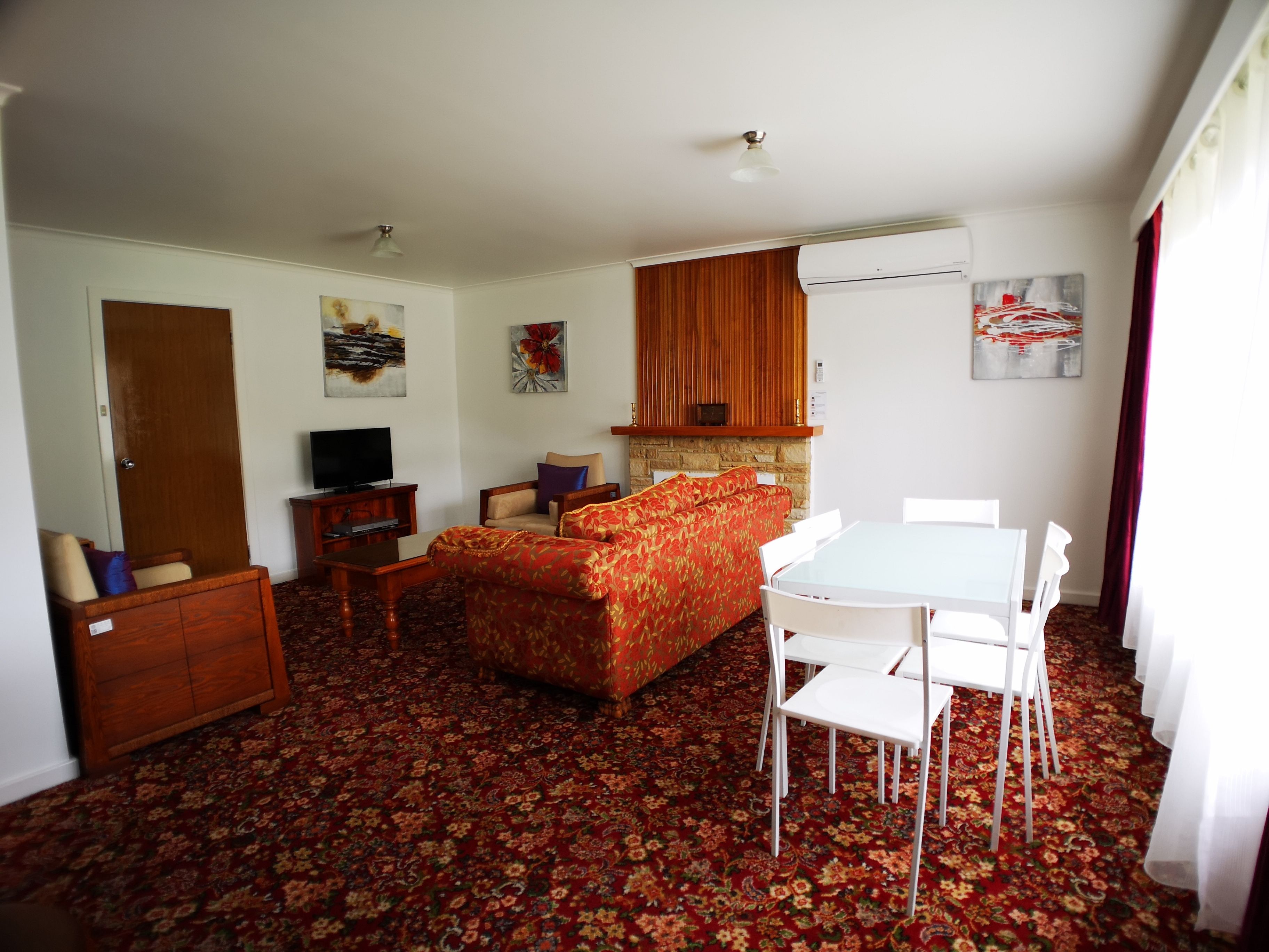 A room with a sofa, a TV, a dining table with chairs, and a patterned carpet.