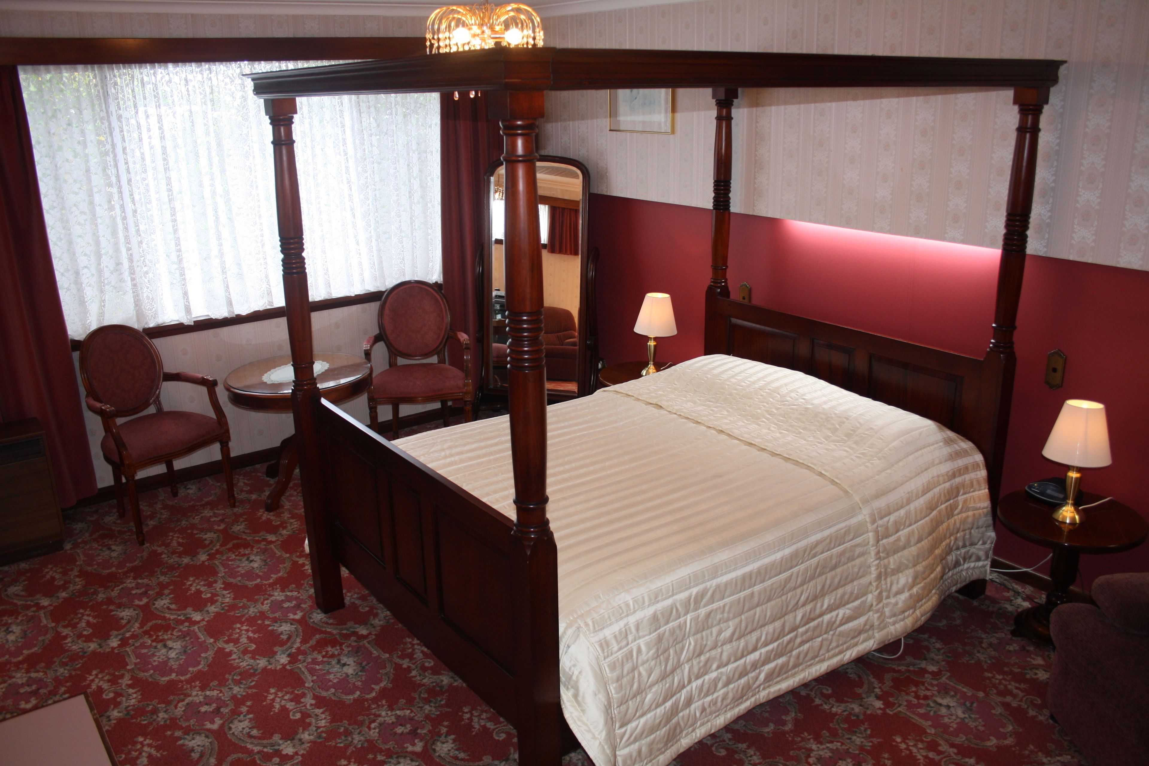 A four-poster bed with a quilt, a round table with a chair, and a mirror on the wall.