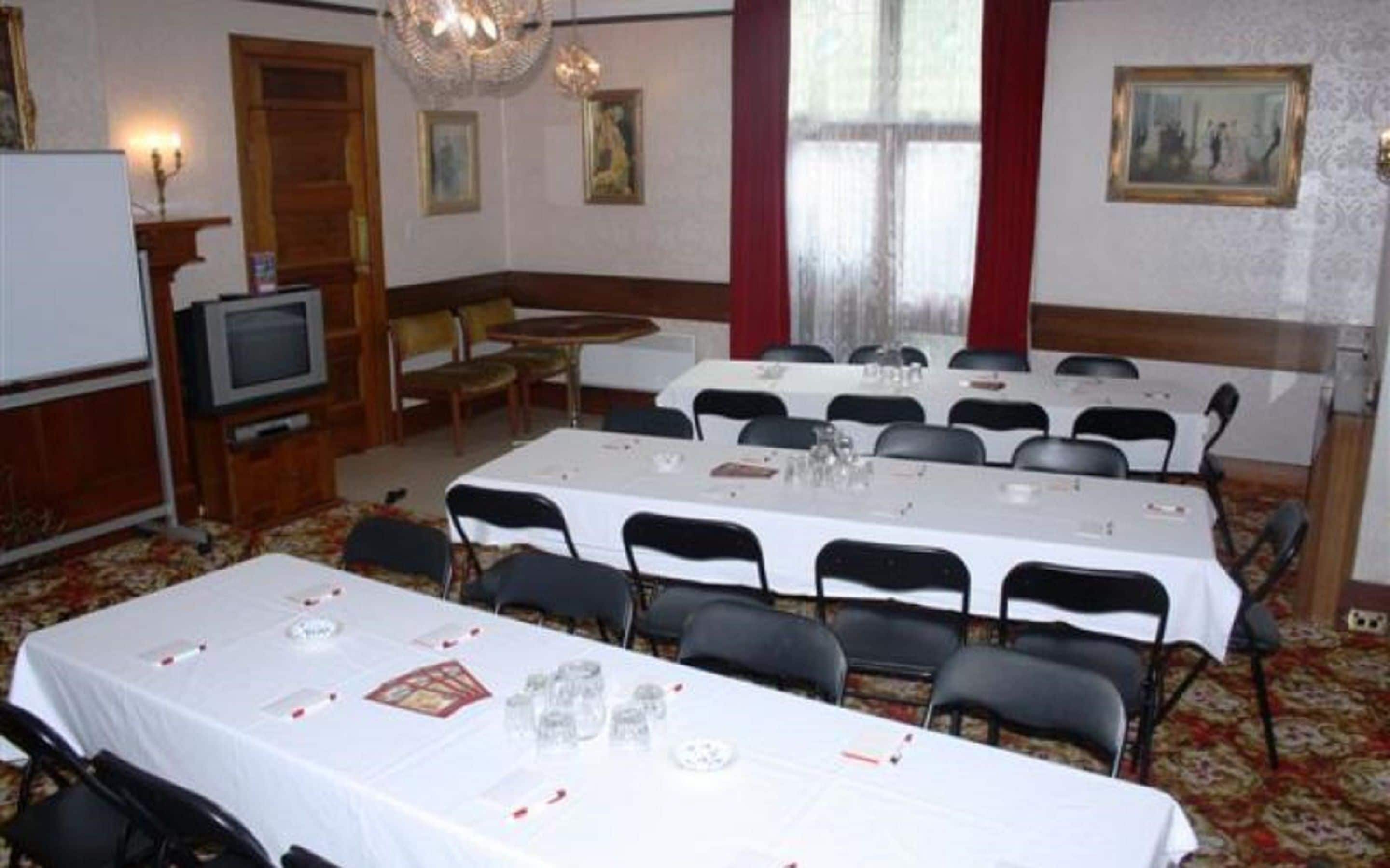 A conference room with multiple tables and chairs, a television, and framed artwork on the walls.