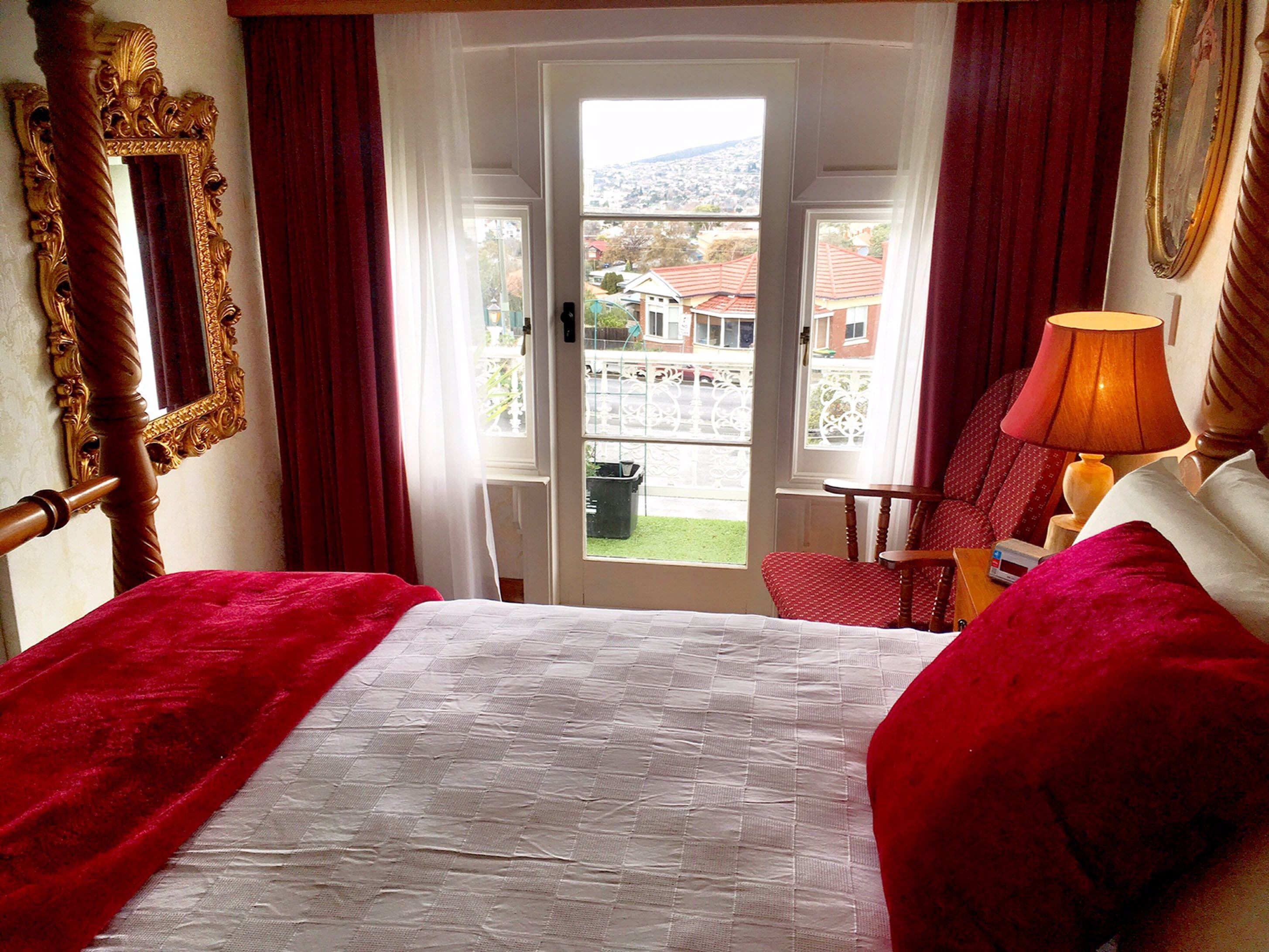 A hotel room with a bed, a chair, a lamp, a mirror, and a view of the outside.