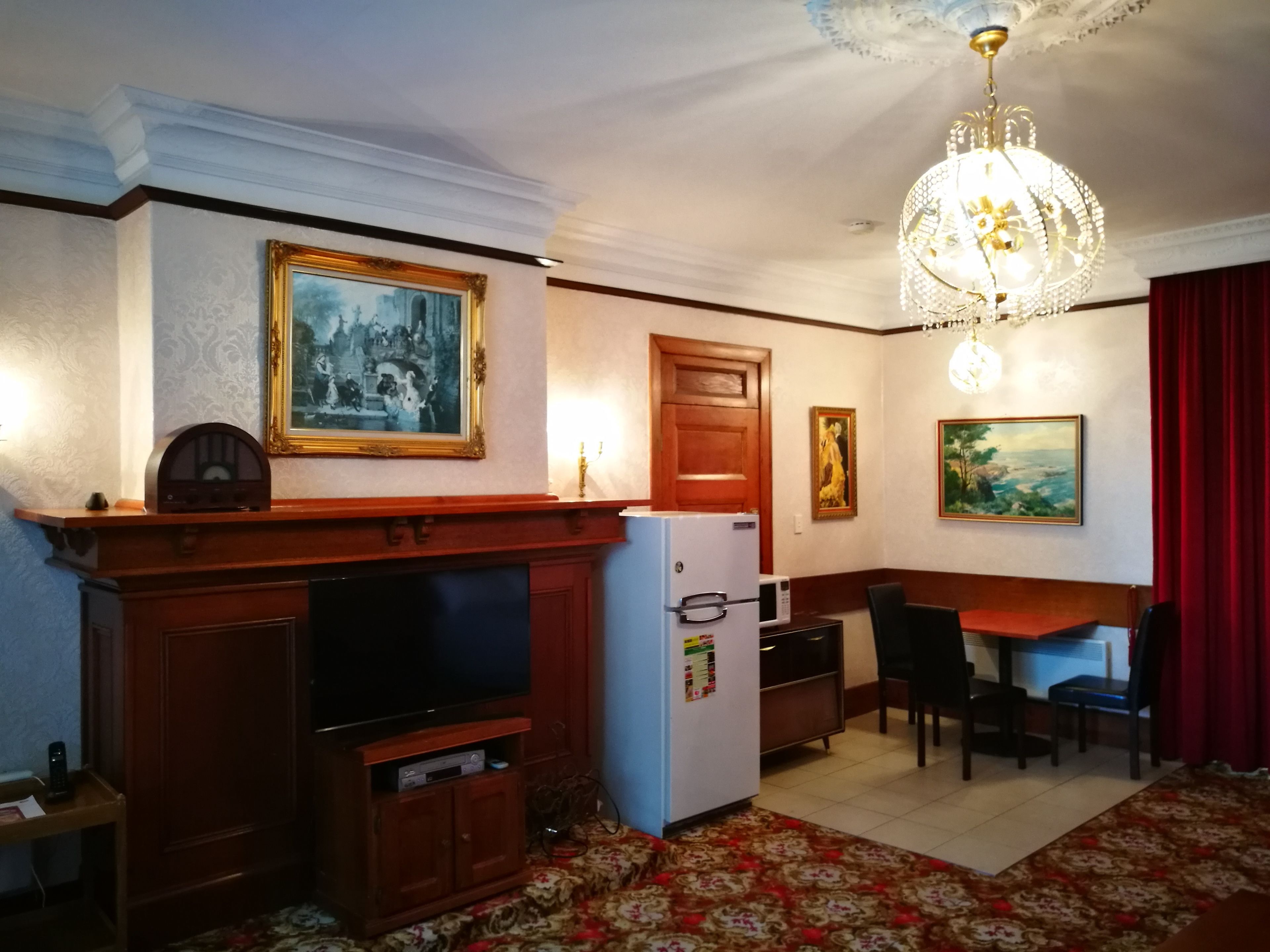 Una sala de estar con chimenea, televisor, refrigerador, mesa de comedor con sillas y candelabro.
