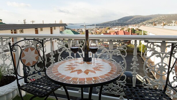 A balcony with a round table and chairs, two wine glasses, and a bottle of wine. - Motel Mayfair on Cavell (West Hobart)