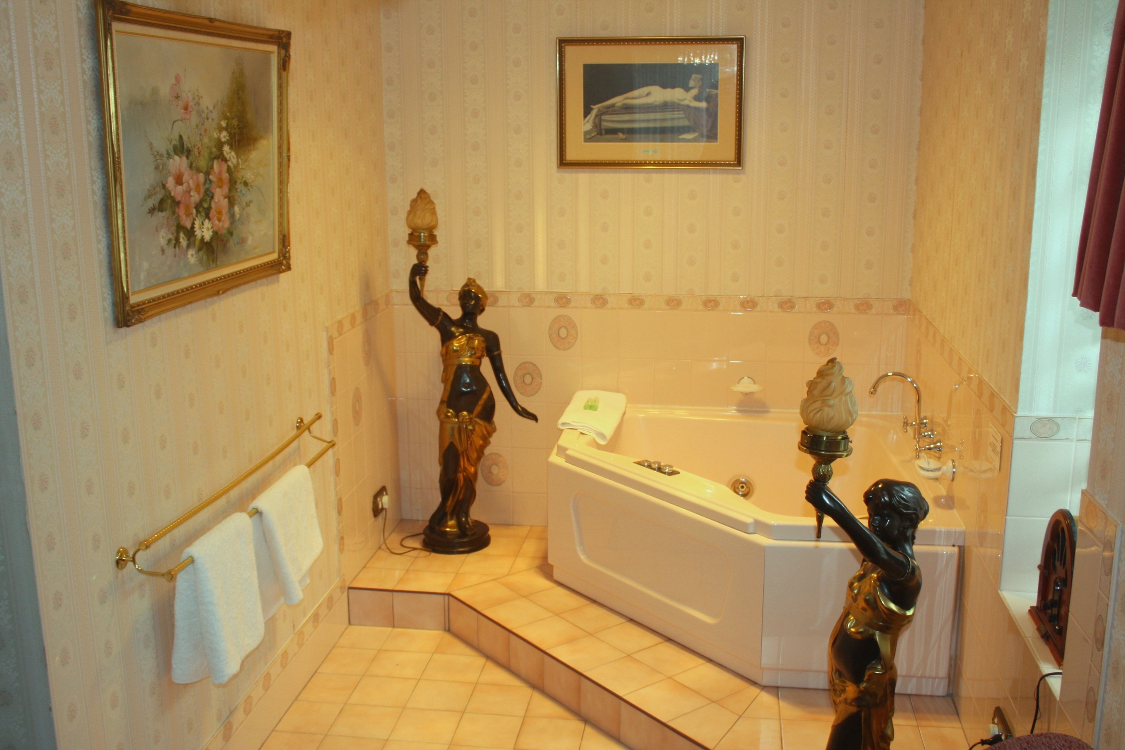 Un baño con una bañera, dos estatuas, un cuadro enmarcado y un perchero para toallas.