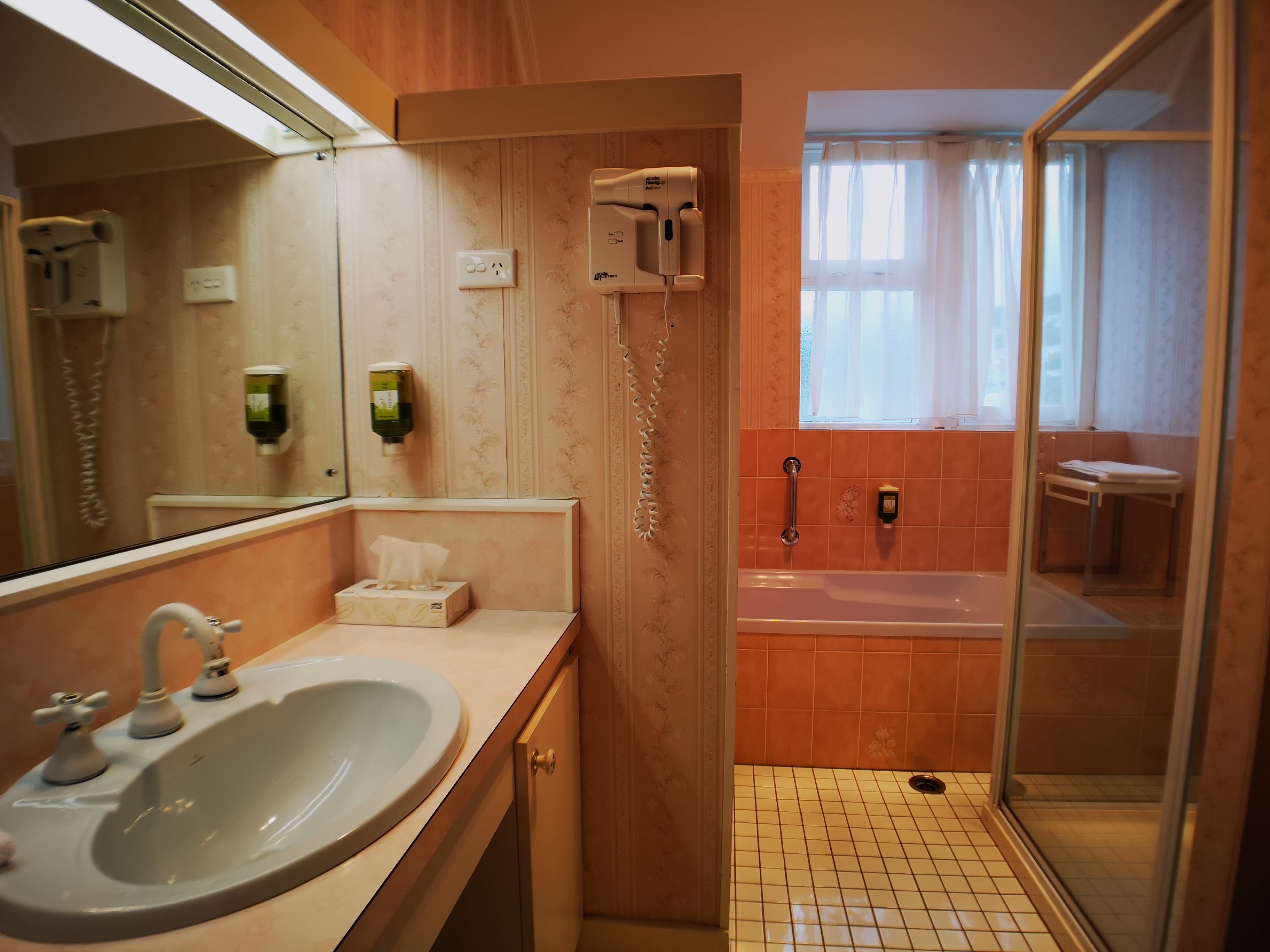 A bathroom with a sink, mirror, hand dryer, and a shower area with a glass door.