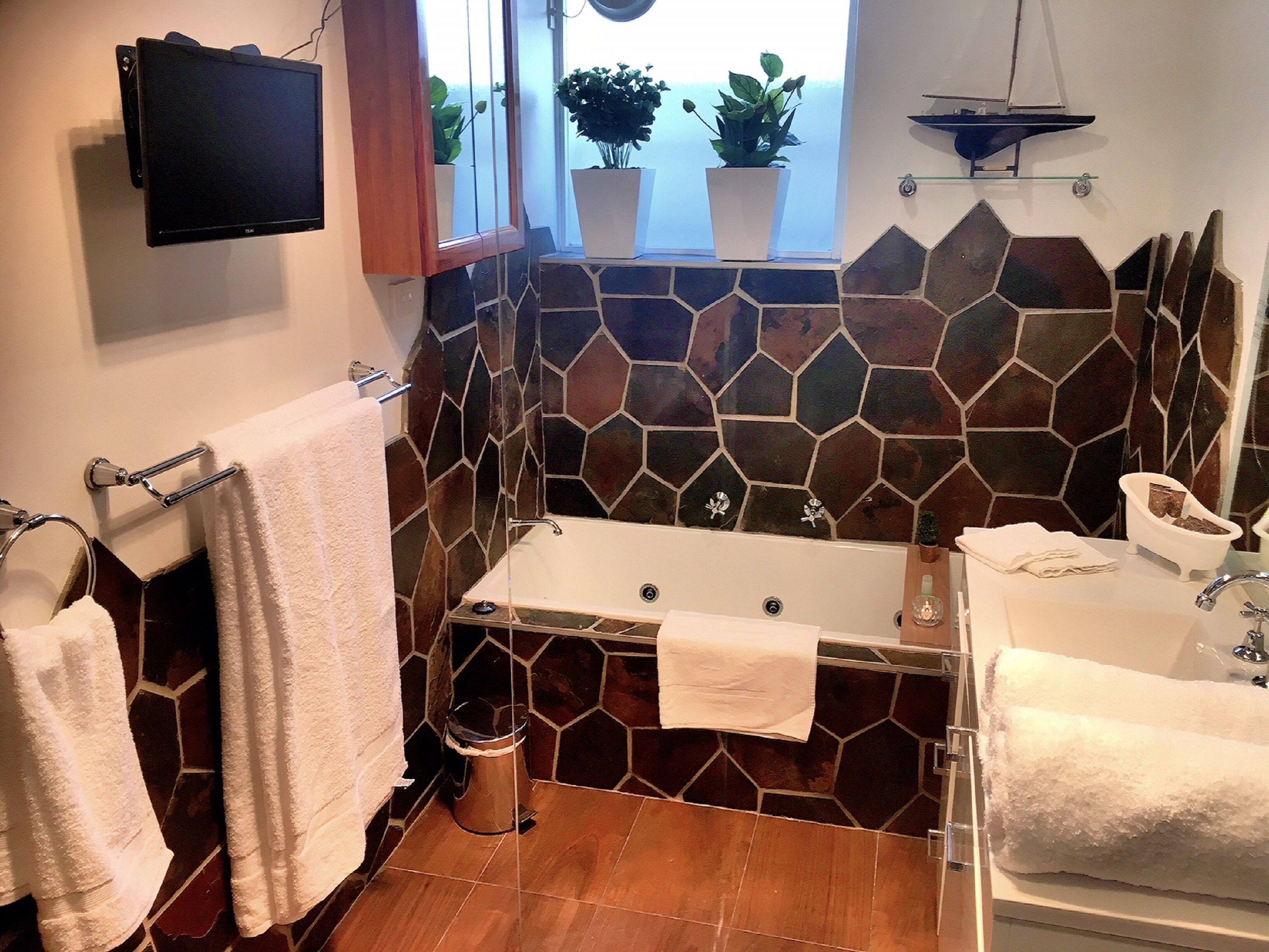 A bathroom with a stone wall, a bathtub, a sink, and a window with plants.