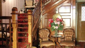 A grand staircase with a wooden handrail, a floral carpet, and two upholstered chairs with a small table between them. - Motel Mayfair on Cavell (West Hobart)