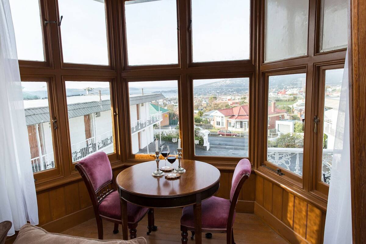 A corner room with a large bay window, a round wooden table, and two chairs.