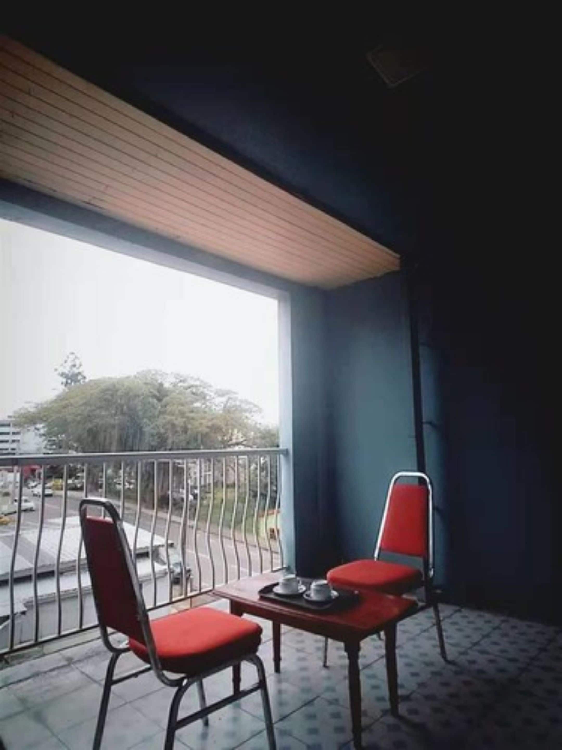 Un balcón con dos sillas rojas y una mesa, vista a la calle y suelo de baldosas.
