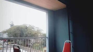 Un balcón con dos sillas rojas y una mesa, vista a la calle y suelo de baldosas.