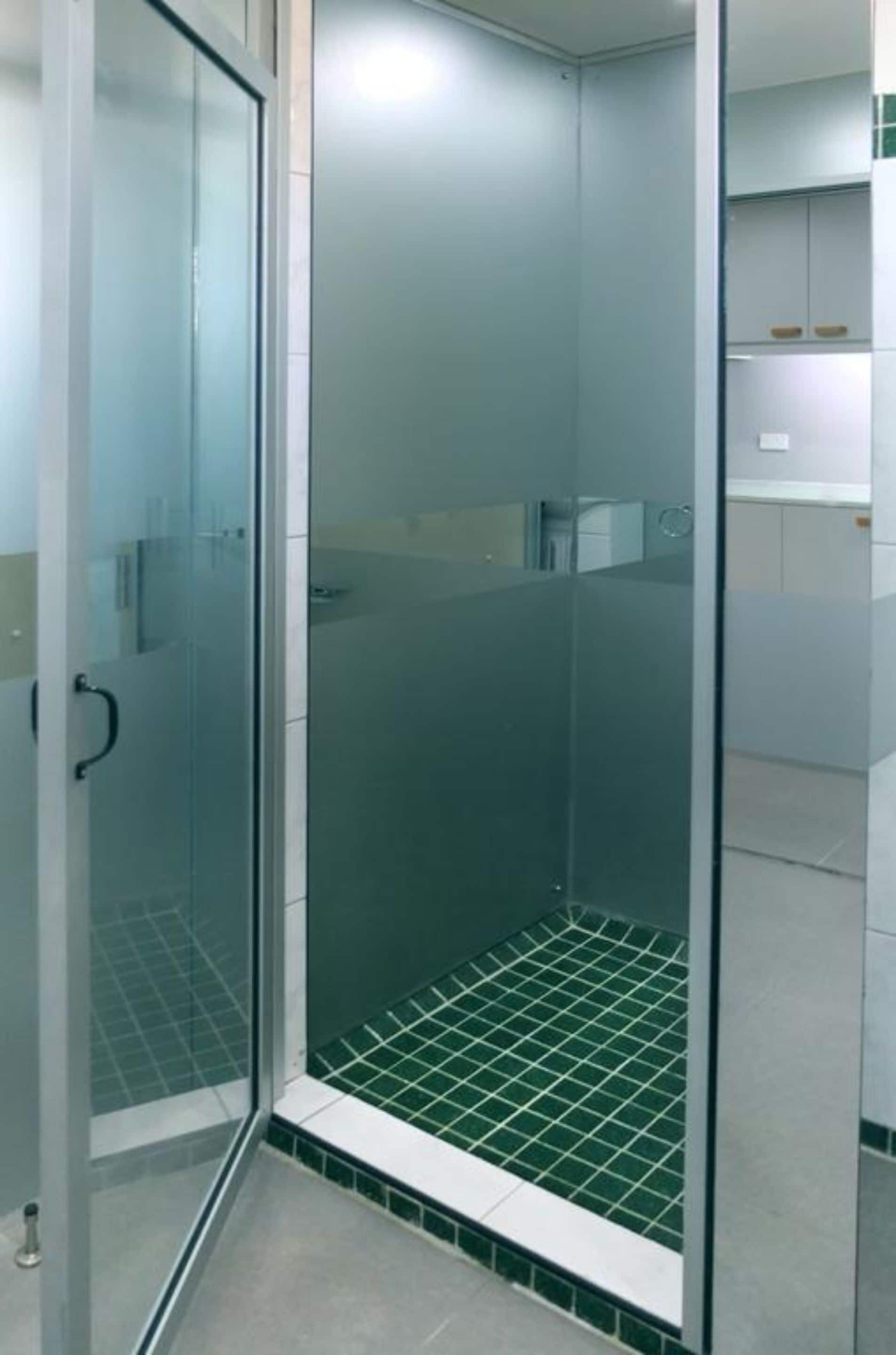 A glass-enclosed shower with a tiled floor and a white door.
