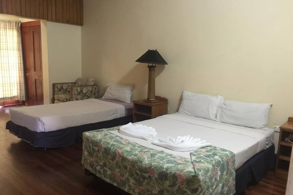 A hotel room with two beds, a nightstand, a lamp, and a window with curtains.