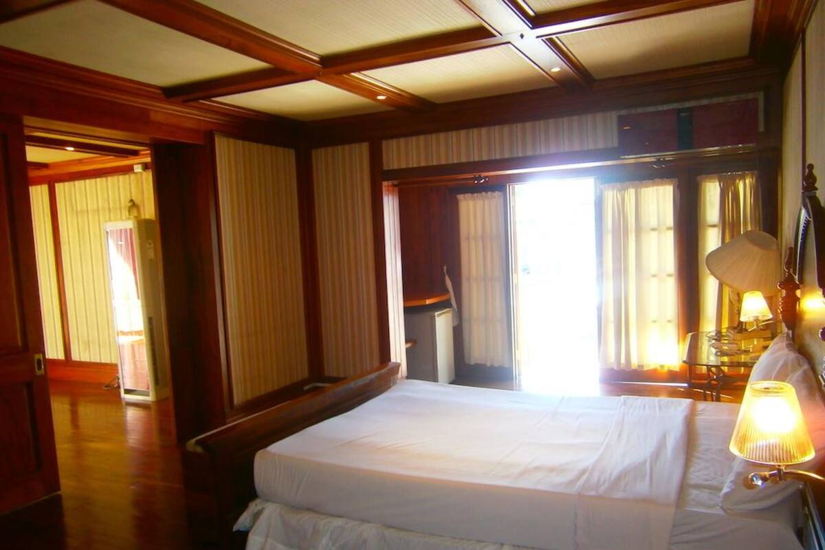 A hotel room with a large bed, wooden flooring, and a window with curtains.