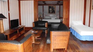 A room with a wooden ceiling, a bed with a blue skirt, a sofa, a television, and a wooden cabinet. - Southern Cross Hotel Fiji (Suva)