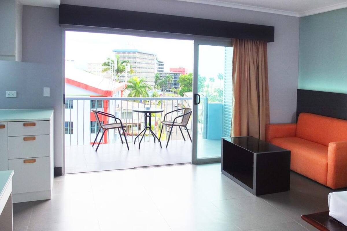 A modern hotel room with a balcony, a sofa, a desk, and a dining area.
