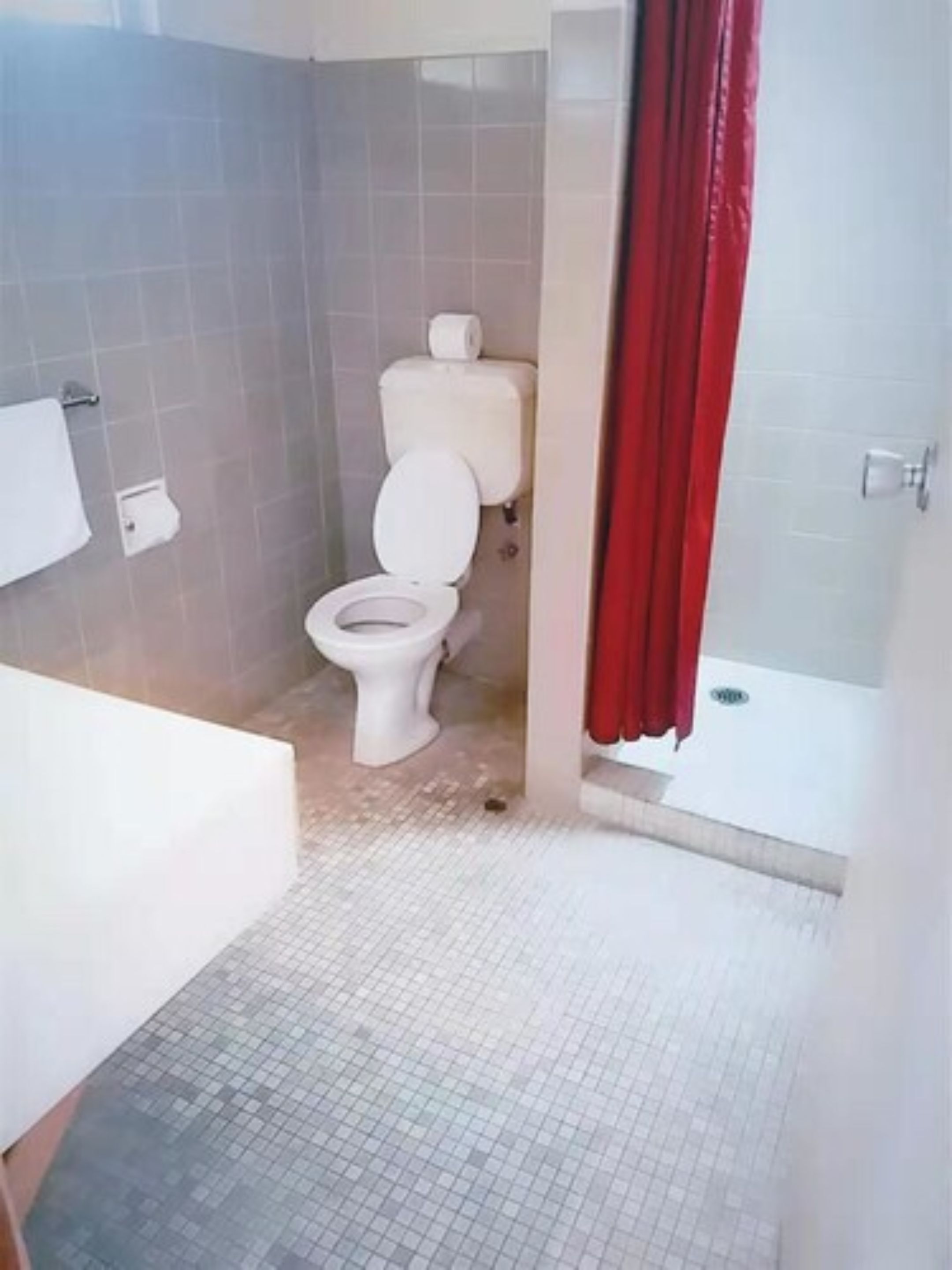 Un baño con inodoro, zona de ducha y suelo de baldosas.