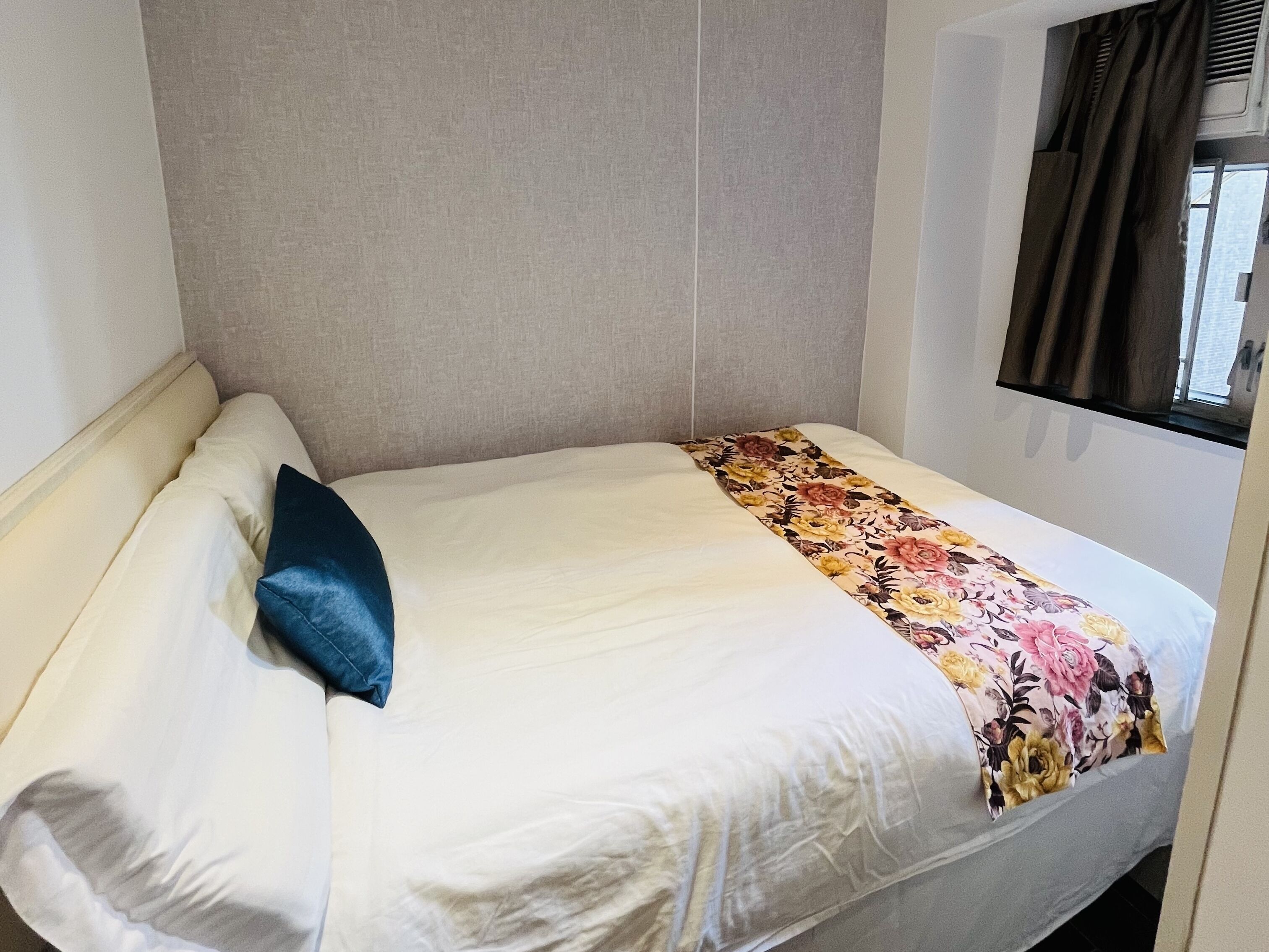 Un lit simple avec une couvre-lit à motifs floraux, un oreiller bleu et une tête de lit.
