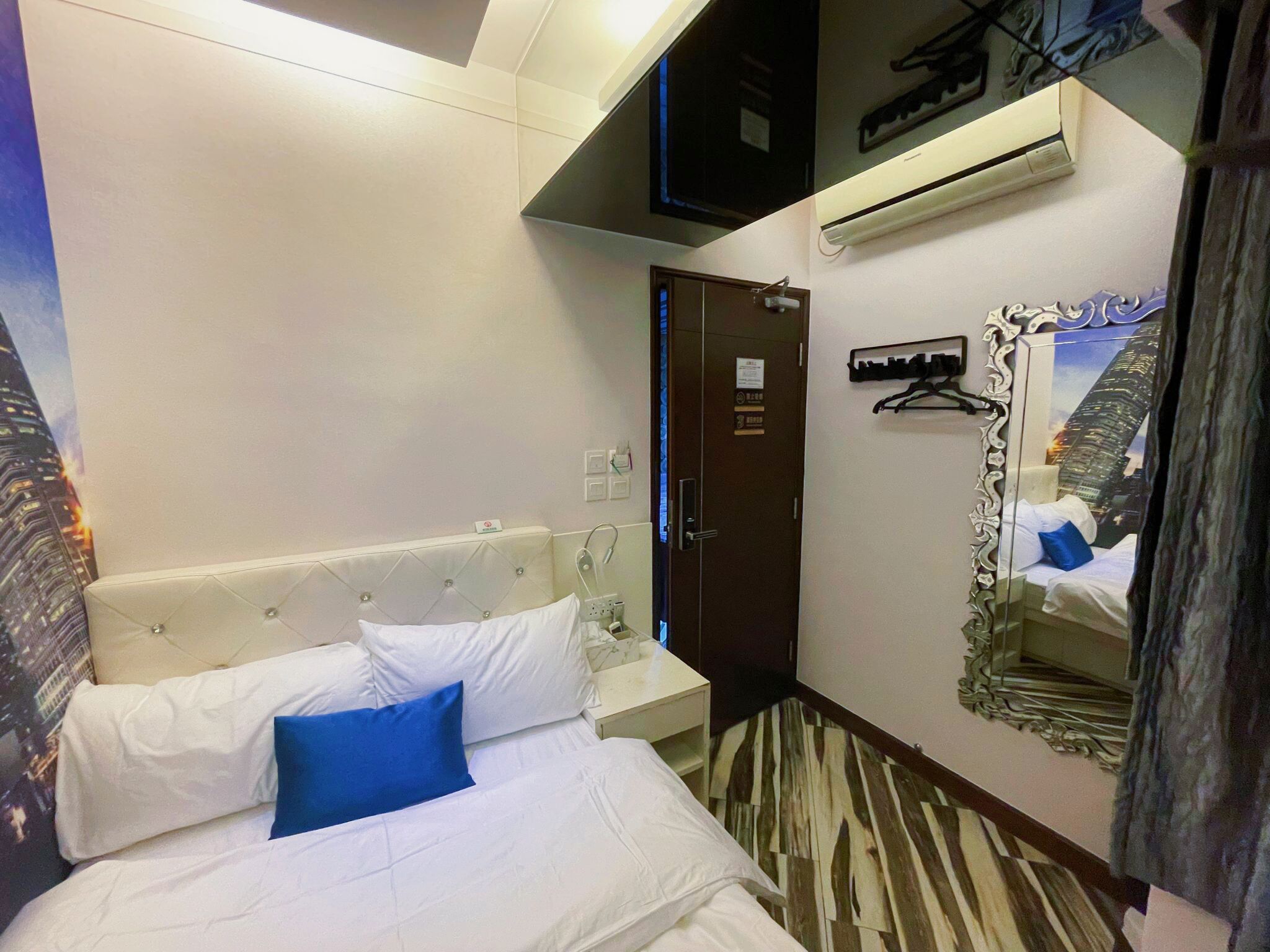 Ein Hotelzimmer mit Bett, Schrank, Klimaanlage und Spiegel mit Blick auf die Stadt.