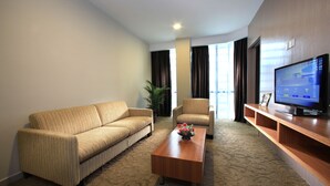 A hotel room with a sofa, armchair, coffee table, TV, and a large window with curtains. - Izumi Hotel Bukit Bintang (Kuala Lumpur)