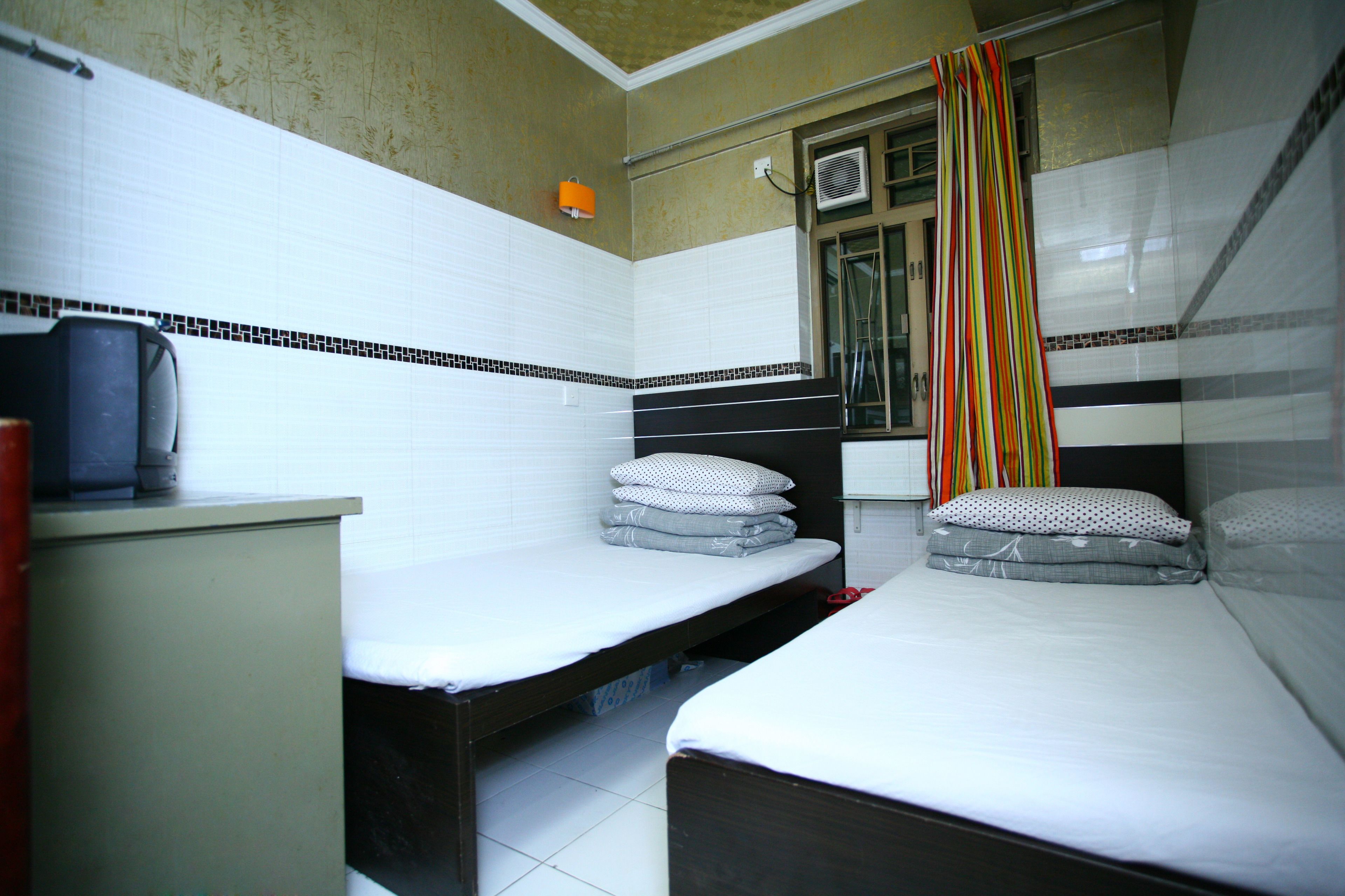 A small, compact room with two single beds, a small desk, and a window with a curtain.