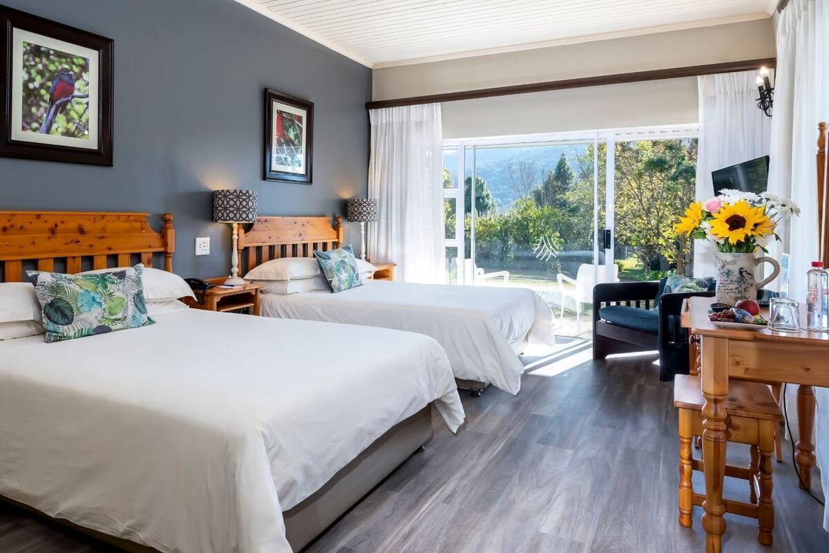 Habitación de hotel con dos camas, un escritorio, una silla y vista al exterior.