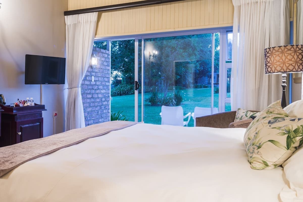 Un dormitorio con una cama grande, un escritorio con un televisor de pantalla plana, una lámpara y vistas a un jardín a través de una puerta corrediza de vidrio.