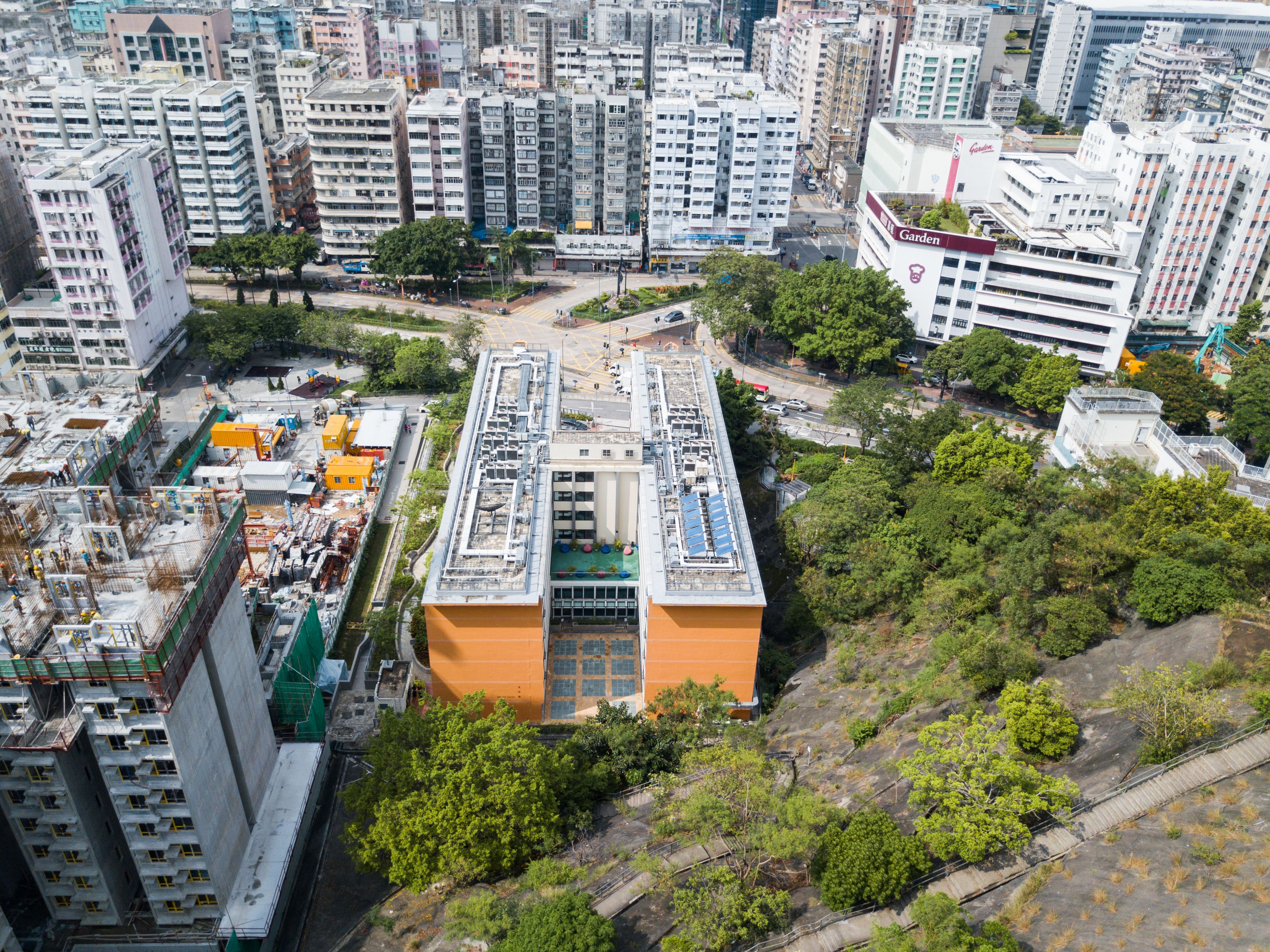 A high-rise building with a rooftop terrace, surrounded by dense urban infrastructure and greenery.