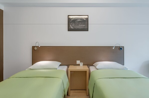 Habitación de hotel con dos camas individuales, cabecera de madera, mesita de noche de madera, un cuadro en la pared y una luz nocturna.