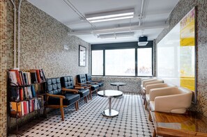 A modern waiting area with a bookshelf, leather seating, and a large window. - YHA Mei Ho House Youth Hostel (Kowloon)
