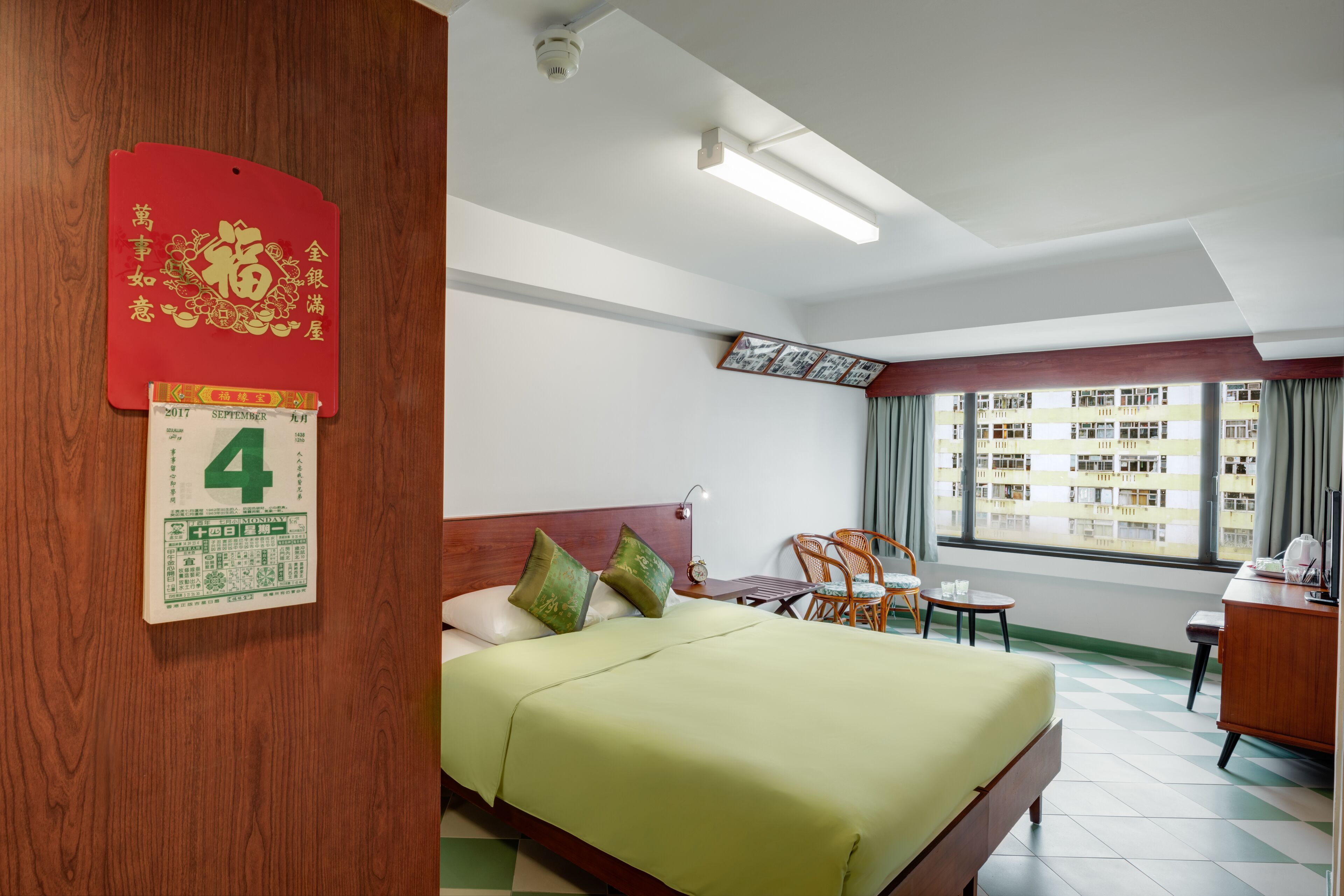 A hotel room with a bed, a desk, a chair, a small table, and a window with a view of buildings.