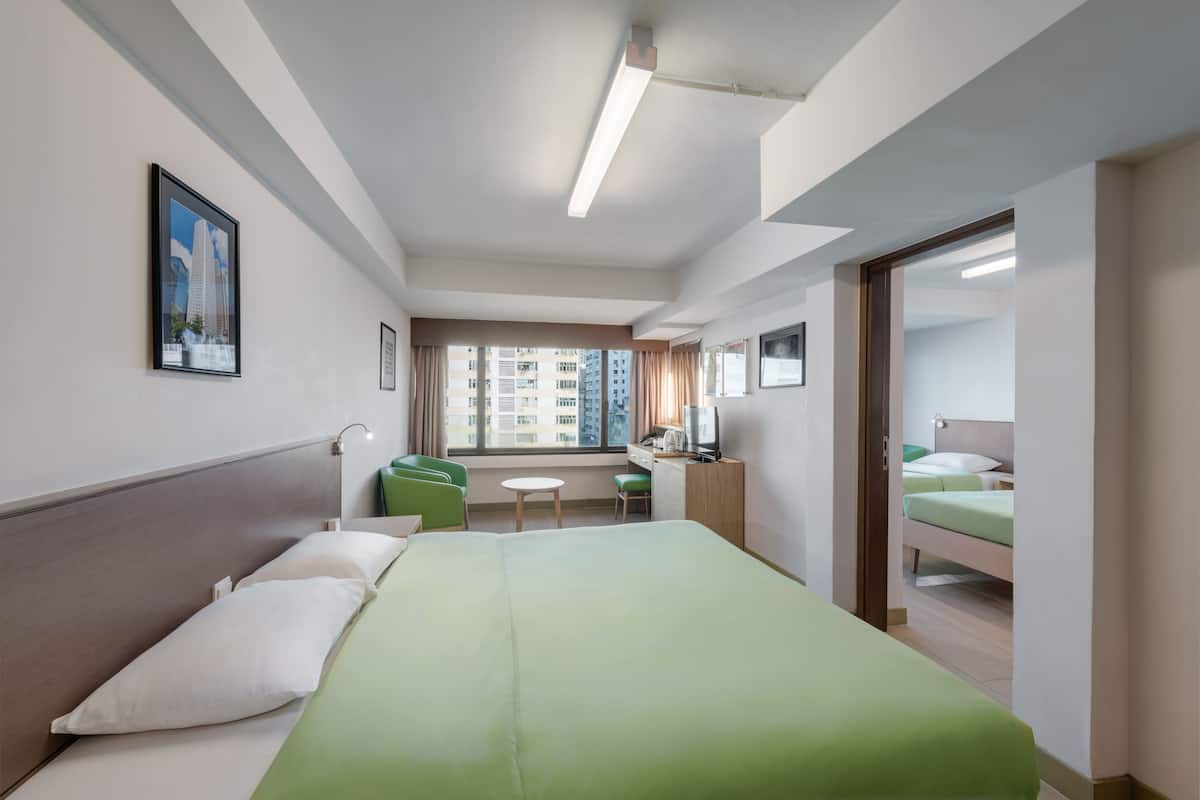 A hotel room with a bed, a desk, a chair, a TV, and a window with a view of buildings.