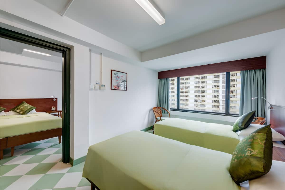 A hotel room with two beds, a window with curtains, a wooden headboard, and a checkered floor.