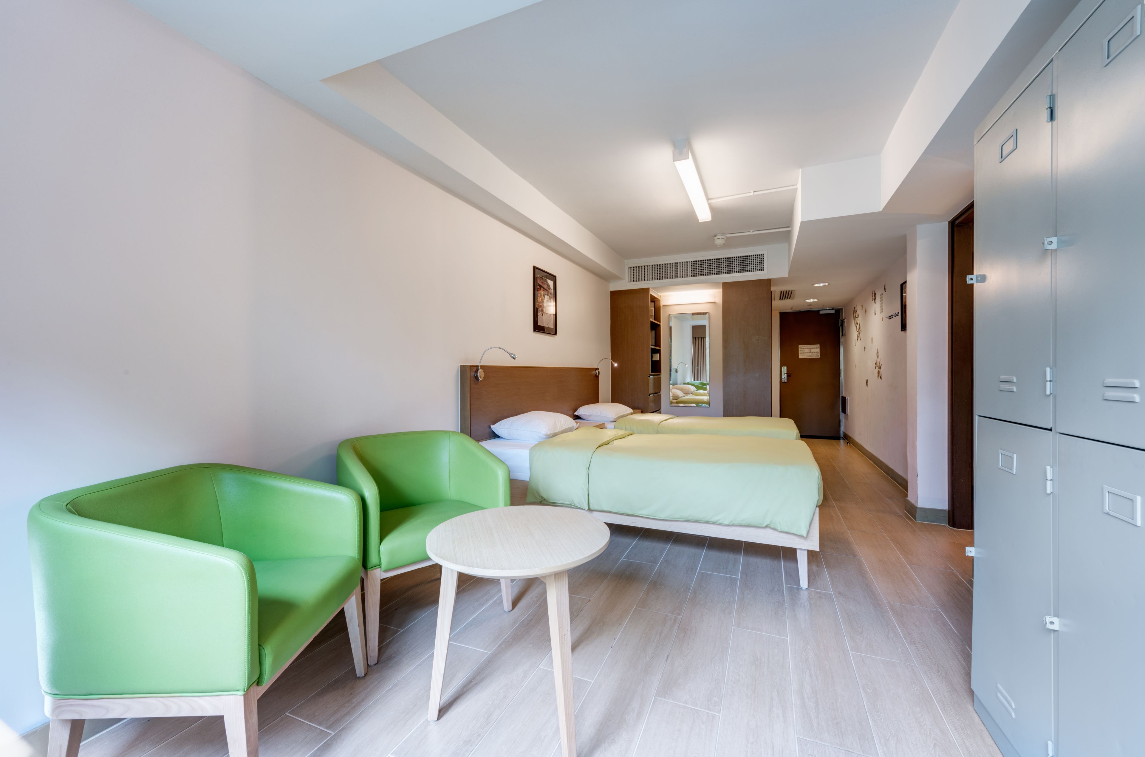 A hotel room with a bed, two green chairs, a small round table, and a wardrobe.
