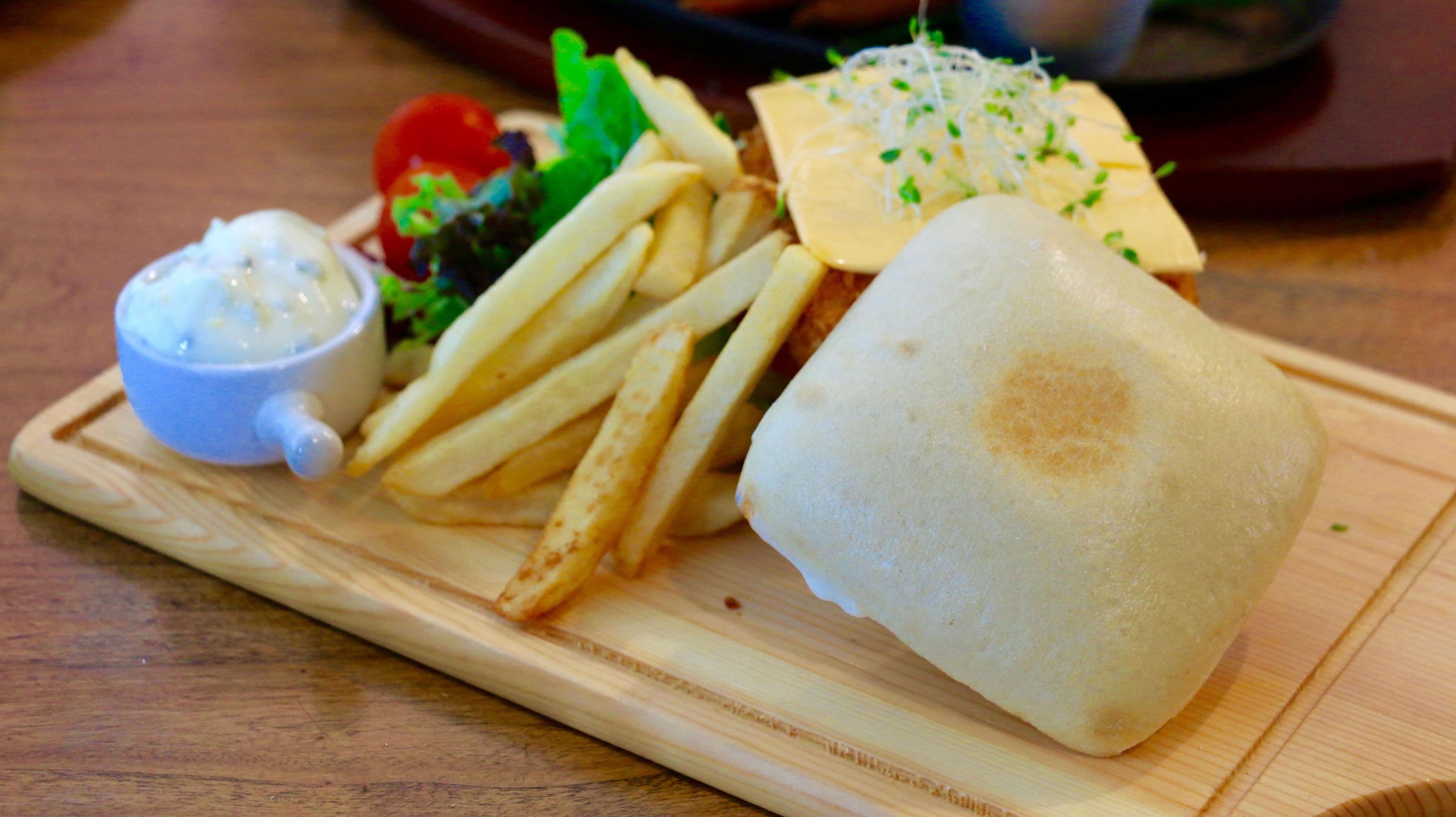A wooden serving tray with a sandwich, fries, a small bowl of sauce, and a salad.