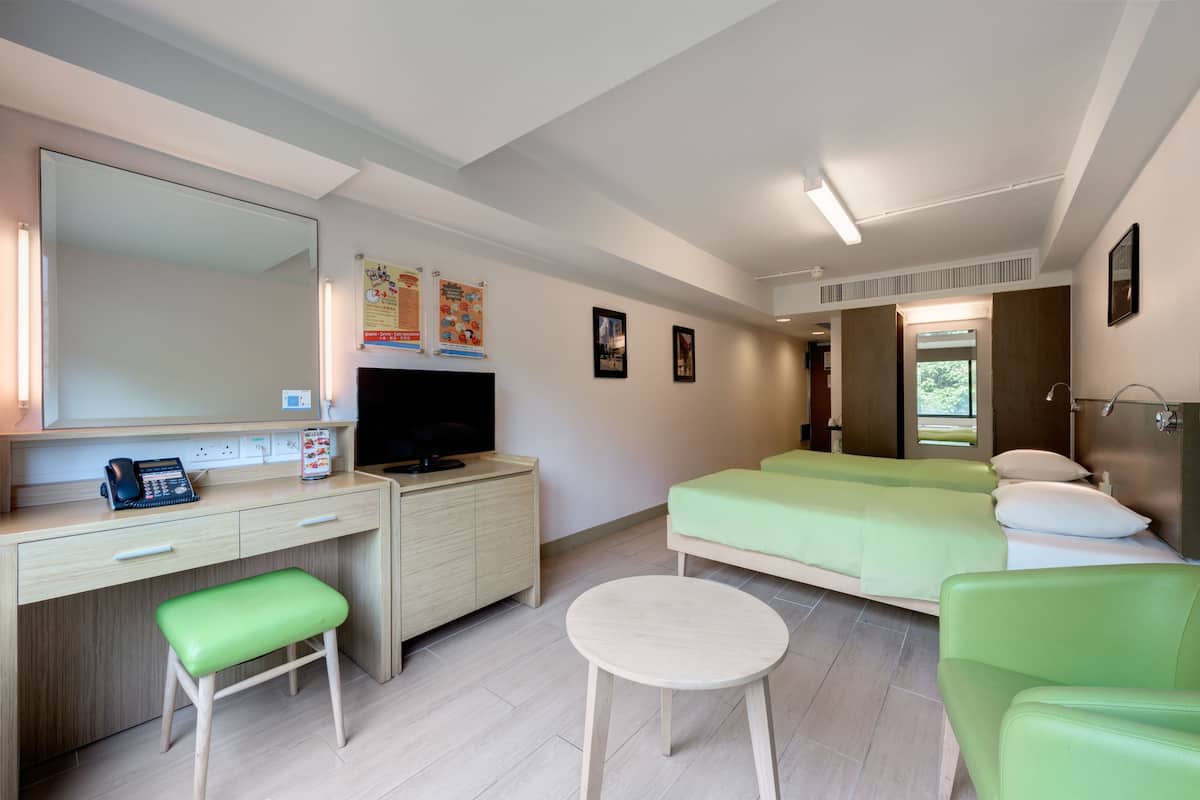 A modern hotel room with a desk, a green sofa, a bed, and a round table.