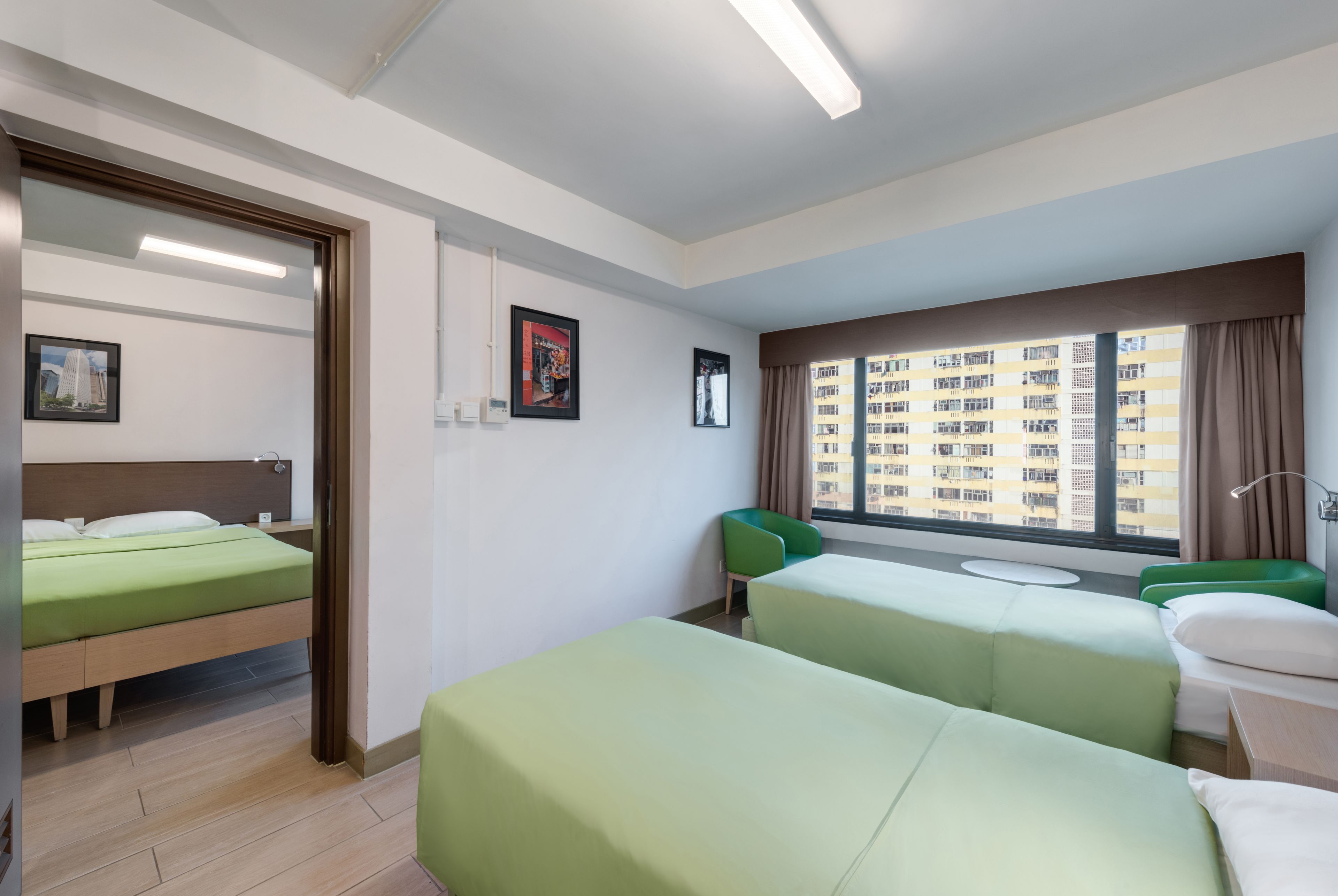 A hotel room with two single beds, a small table, a chair, and a window with a city view.