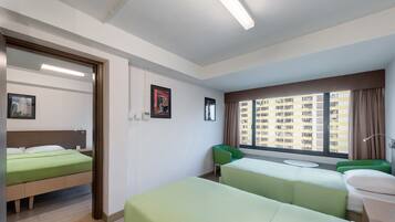 A hotel room with two single beds, a small table, a chair, and a window with a city view.