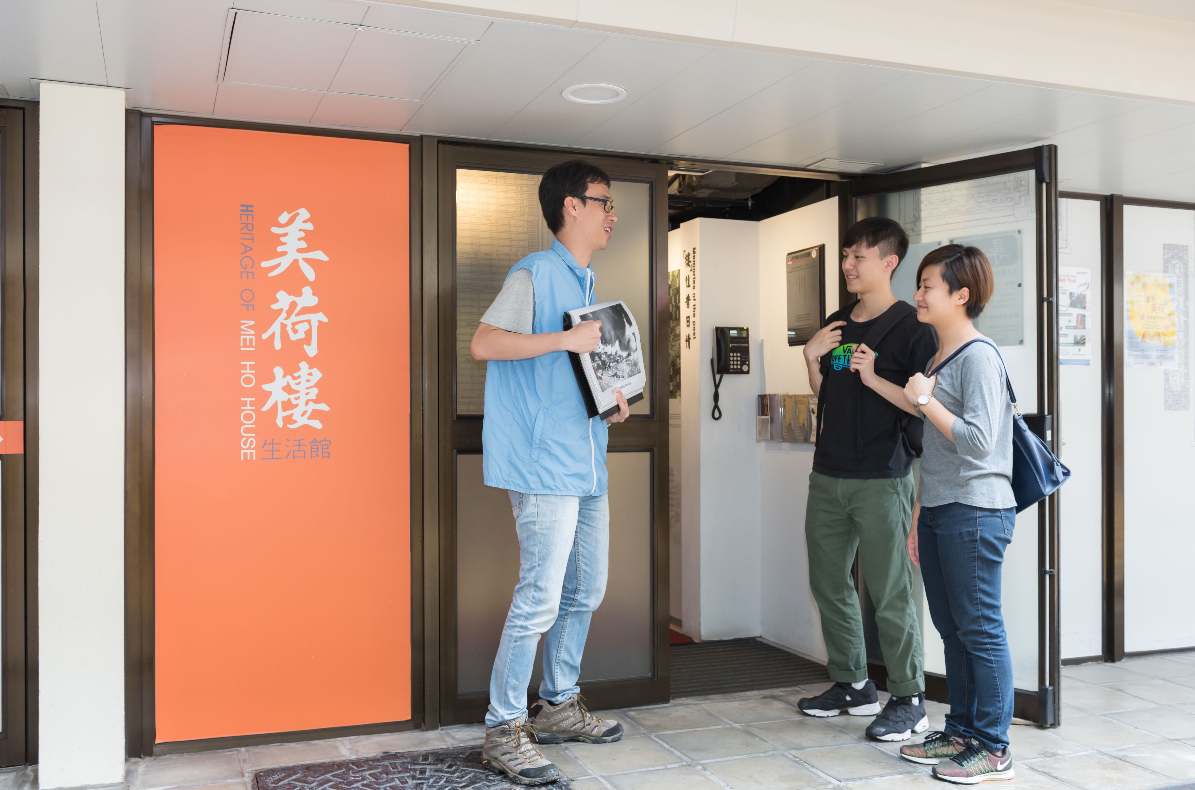 A hotel entrance with a sign reading "MEI HO HOUSE" and a person holding a photo.