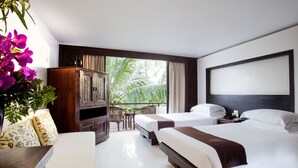 A hotel room with two beds, a wooden cabinet, a desk, and a view of palm trees. - Safari Beach Hotel (Patong)