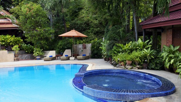 A swimming pool with a blue tiled edge, surrounded by lush greenery and a covered seating area. - Safari Beach Hotel (Patong)