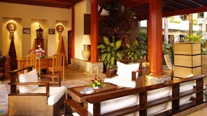 A lobby with wooden furniture, a stone fireplace, and tropical plants. - Safari Beach Hotel (Patong)