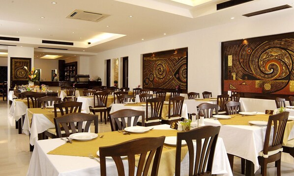 A restaurant with multiple tables and chairs, each set with white tablecloths and gold placemats. - Safari Beach Hotel (Patong)